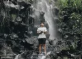 Wisatawan laki-laki dengan baju putih berdiri di bebatuan air terjun Batu Santek