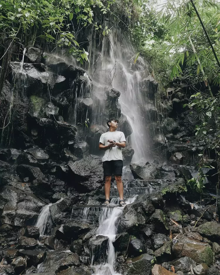 Wisatawan laki-laki dengan baju putih berdiri di bebatuan air terjun Batu Santek
