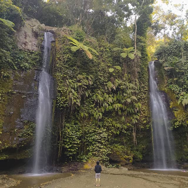 Seorang wisatawan berdiri menikmati keindahan dua air terjun yang mengalir