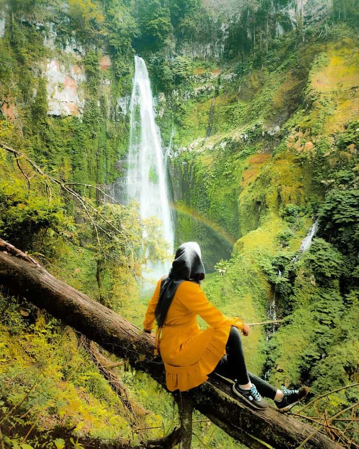 Seorang Wisatawan wanita duduk menatap kearah air terjun