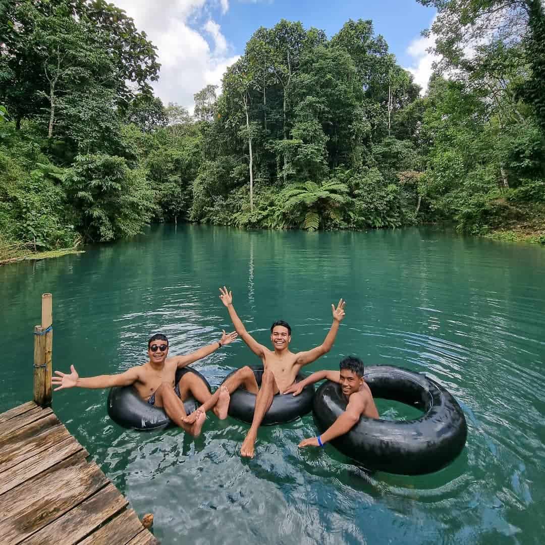 Tiga wisatawan berenang dengan ban karet di tepi Danau Biru