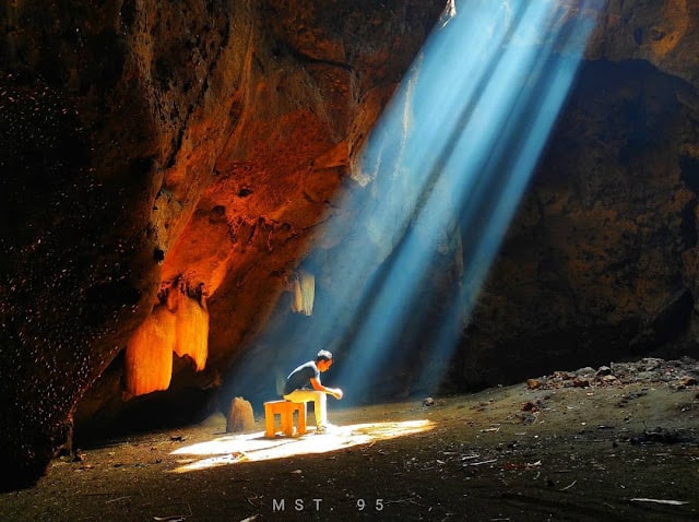 seorang pria duduk di bawah sinar cahaya matahari di dalam gua sumur