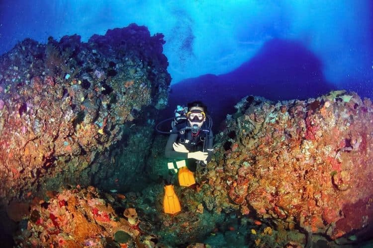 penyelam berada di dasar laut dan dikelilingi terumbu karang di laut Pantai Belongas