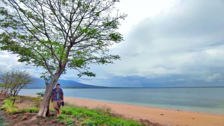 Wisatawan berdiri dibawah pohon dengan pemandangan laut dan pasir putih di Gili Bidara