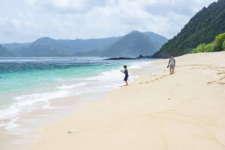 Wisatawan bermain dipinggir Pantai Mawi dengan pemandangan air laut biru