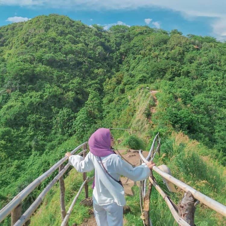 Wisatawan perempuan berada di atas bukit hijau dengan baju putih