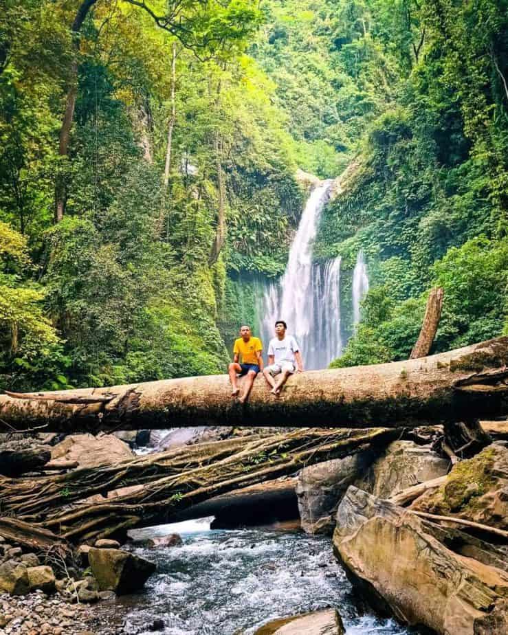 Dua wisatawan duduk di batang kayu besar diatas aliran sungai