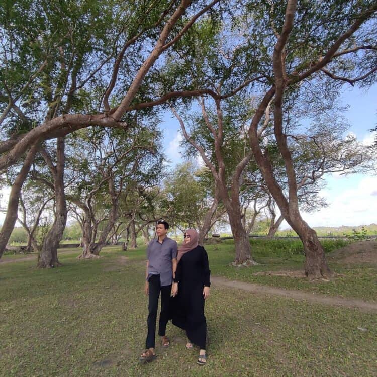 Dua wisatawan berada di bawah pepohonan hijau