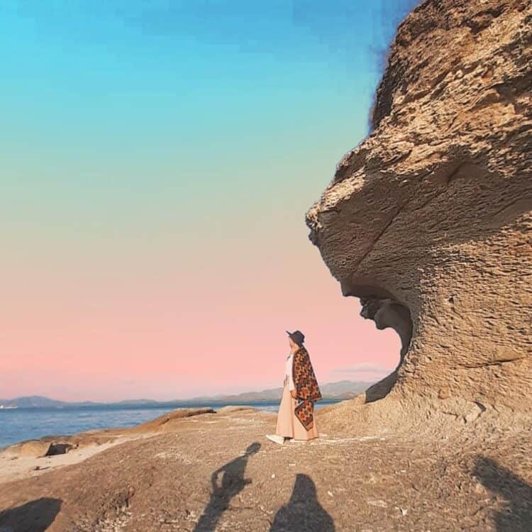 Wisatawan berdiri di bawah batu karang yang tinggi
