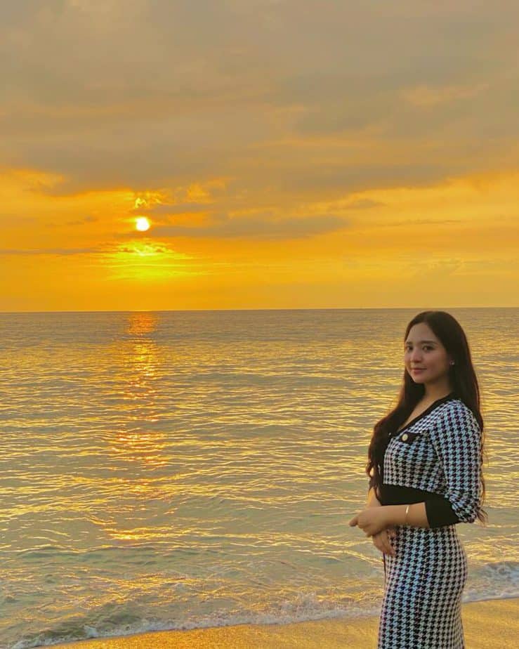 Wanita berdiri di tepi pantai dengan warna langit jingga