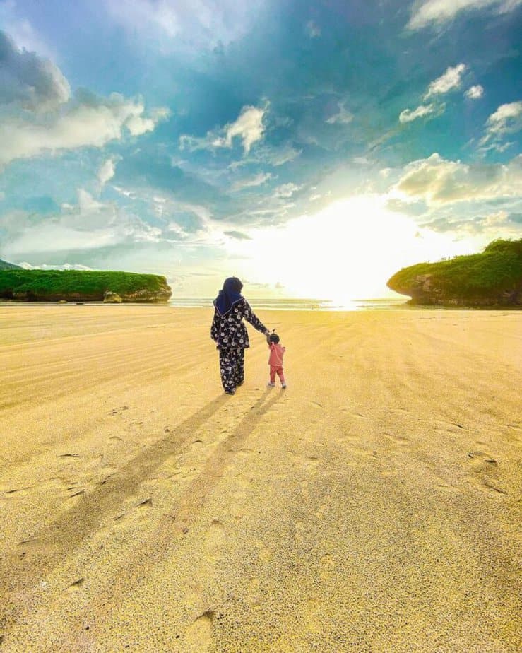 Seorang ibu dan anaknya berjalan di hamparan pasir pantai