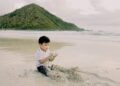 Anak kecil bermain pasir di pinggir pantai