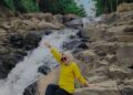 Wisatawan perempuan dengan baju kuning bersantai di aliran Air Terjun Rora
