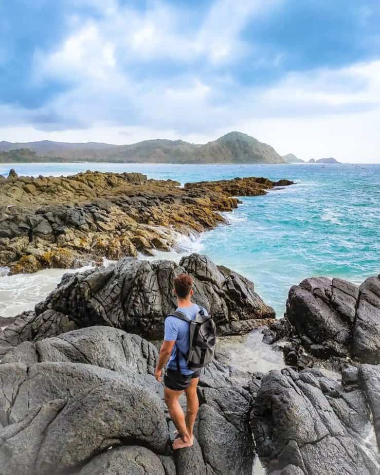 Wisatawan berdiri memandangan lautan di atas batuan alam tepi pantai