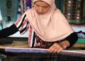 Seorang ibu sedang melakukan kegiatan tenun kain songket