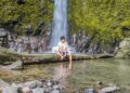 Wisatawan duduk di batang kayu tepi sungai Air Terjun Titian Batu Kawangan