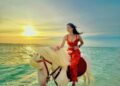 Wisatawan menunggangi kuda di pinggir pantai ketika matahari akan terbenam