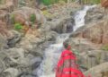 Wisatawan dengen selendang merah berada di depan aliran air terjun