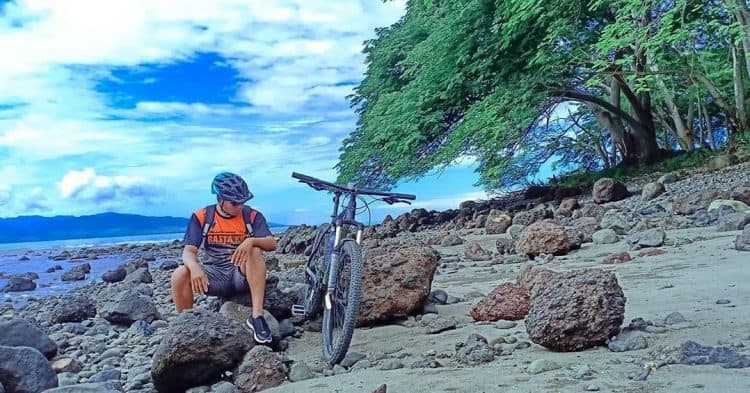 Wisatawan beristirahat di batu karang pantai dengan sepedanya