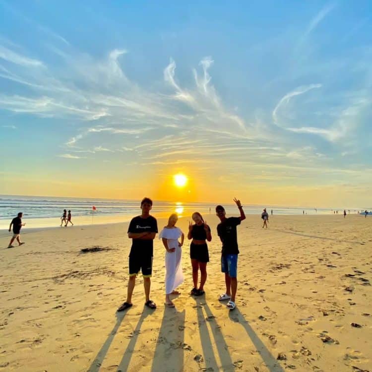 Empat orang berada di kawasan pantai dengan latar belakang matahari yang indah