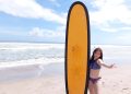 Wisatawan menggunakan bikini memegang papan surfing